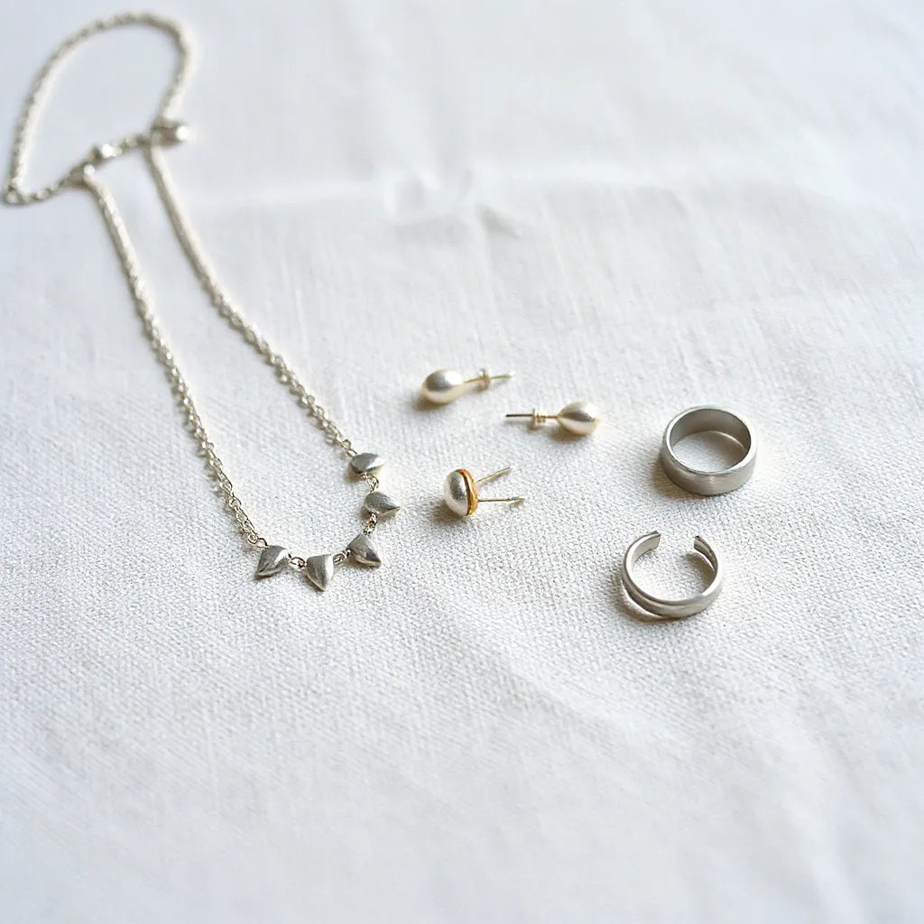 Artisan-made silver necklace, earrings, and ring displayed on a neutral linen background