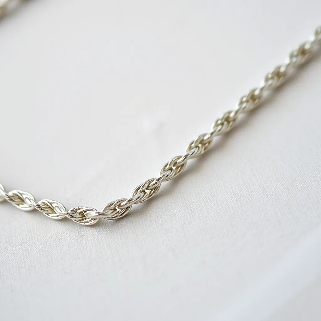 Silver rope chain with clear braided links catching soft light on neutral fabric