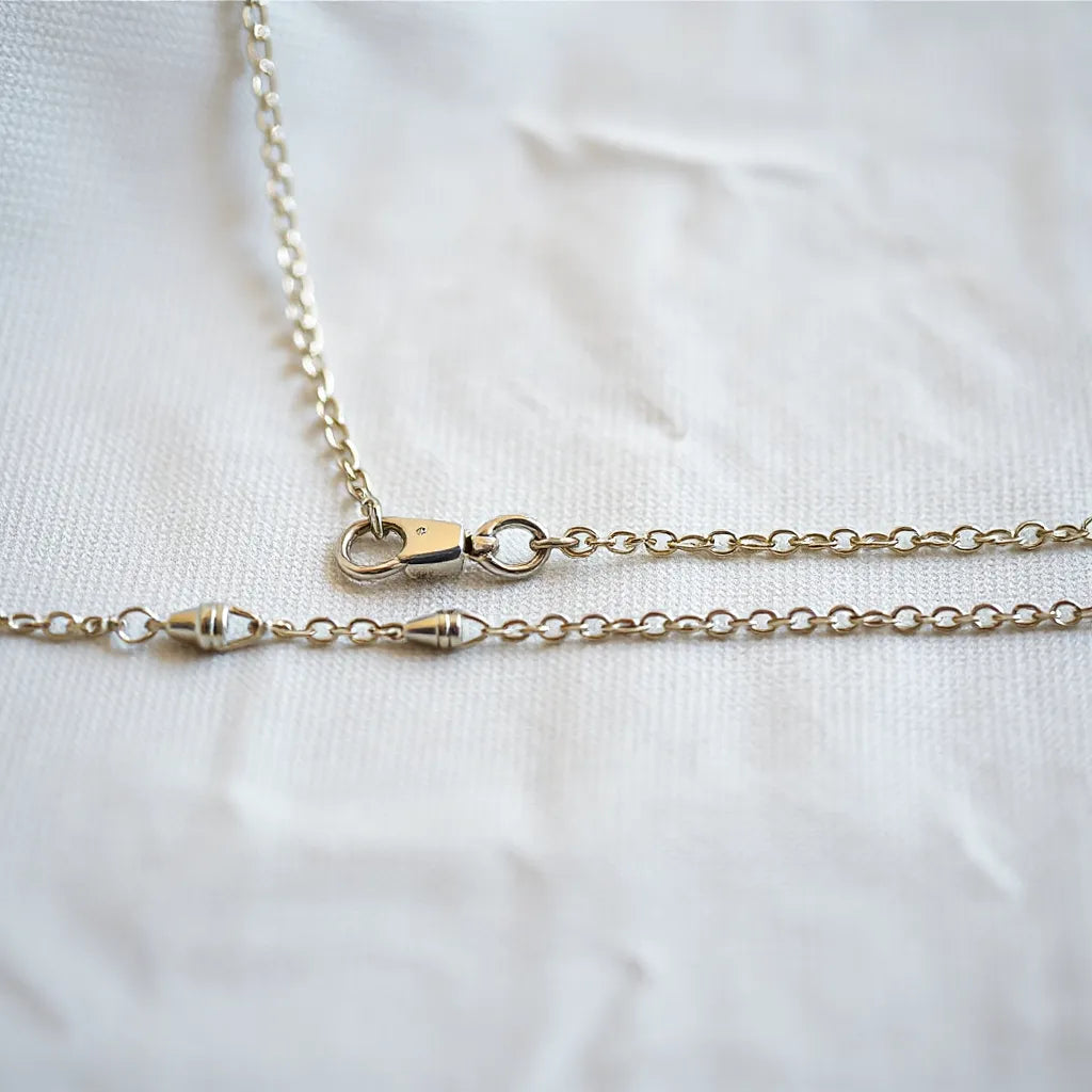 Silver chain with an adjustable length extender on neutral fabric, showing multiple fit lengths