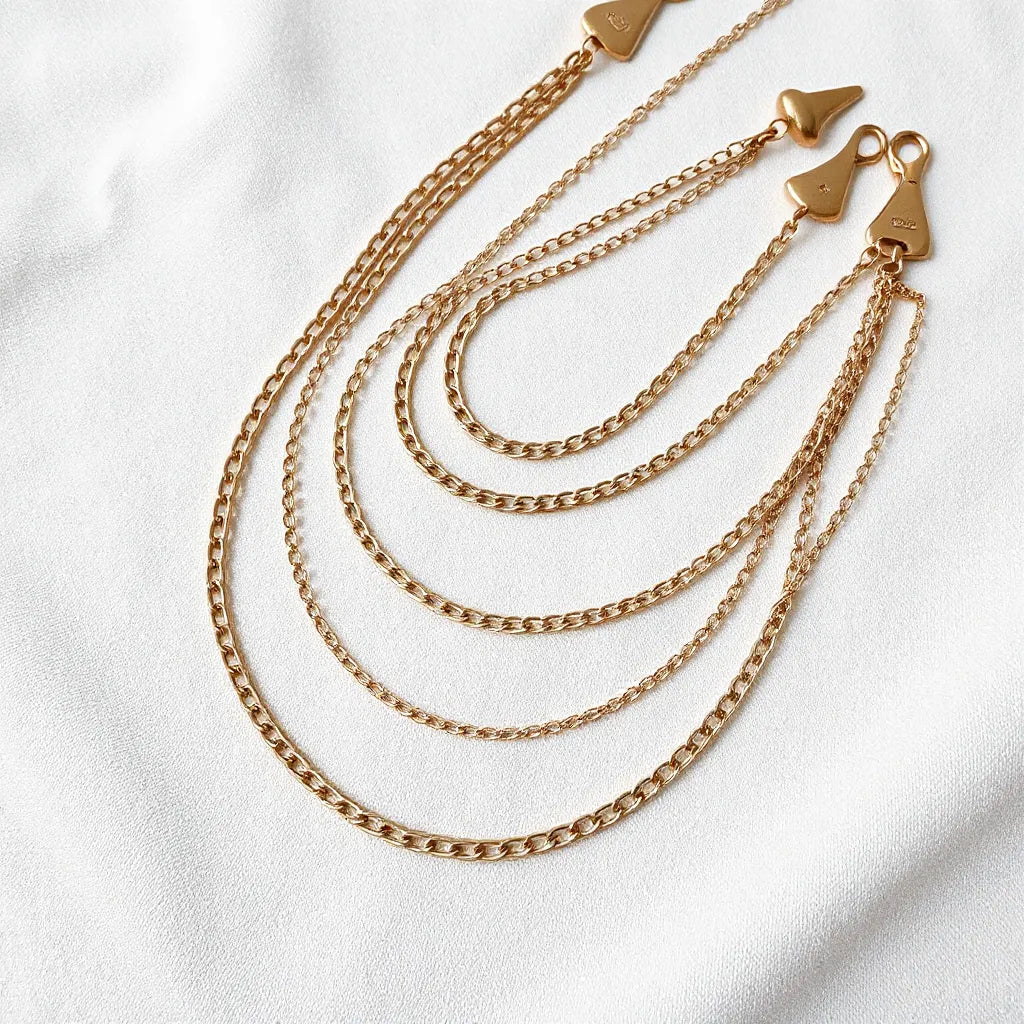 Layered necklaces and bracelets displayed to show different chain lengths on a light fabric background