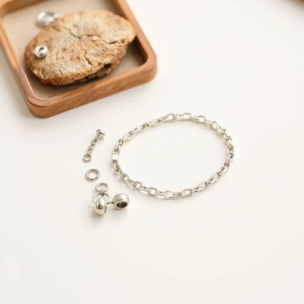 Adjustable silver bracelet with interchangeable links and small charm pieces on a minimal tray