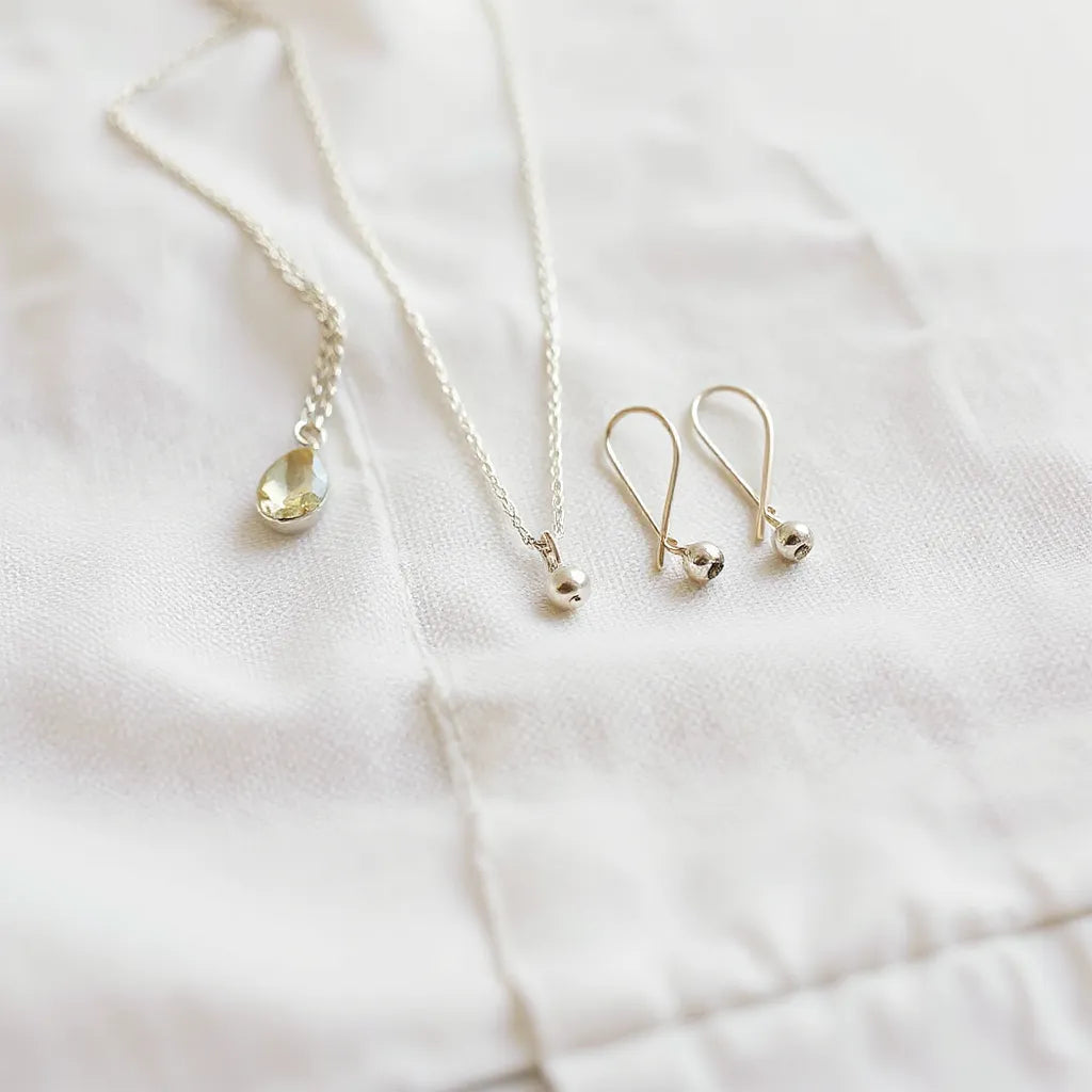Delicate natural silver necklace and earrings on light fabric with soft reflections