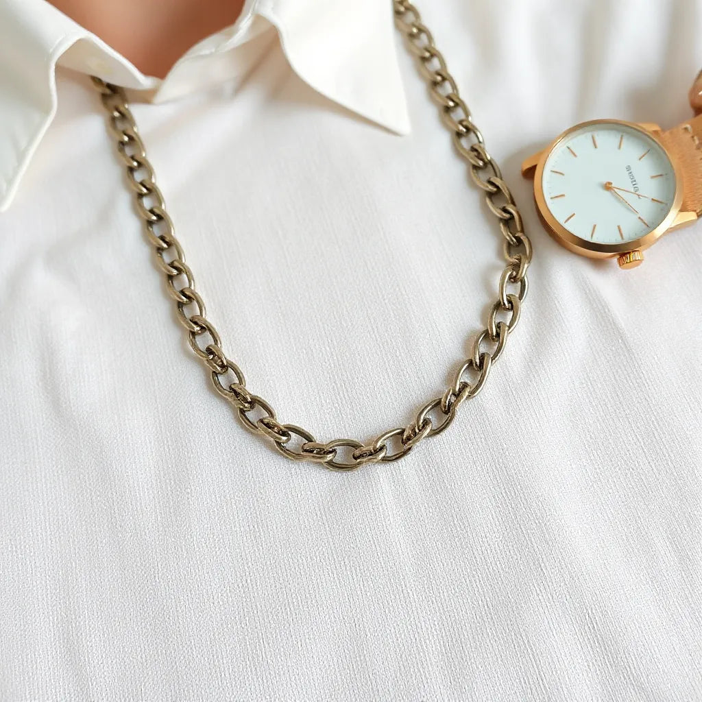 Figaro chain necklace resting on neutral fabric with a white shirt collar in soft focus
