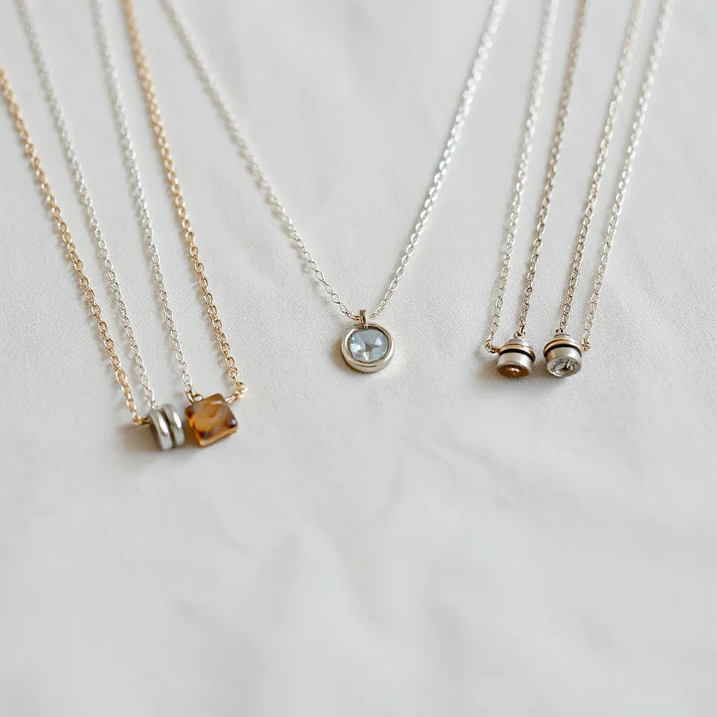 Assorted silver necklaces with delicate chains and a small pendant on neutral fabric