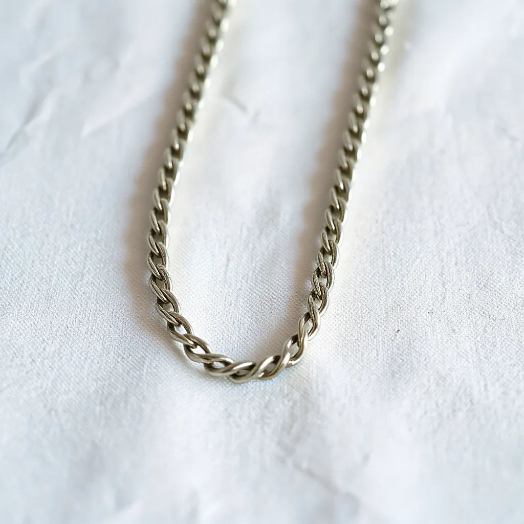 Silver rope chain necklace with detailed braided links on a light neutral background