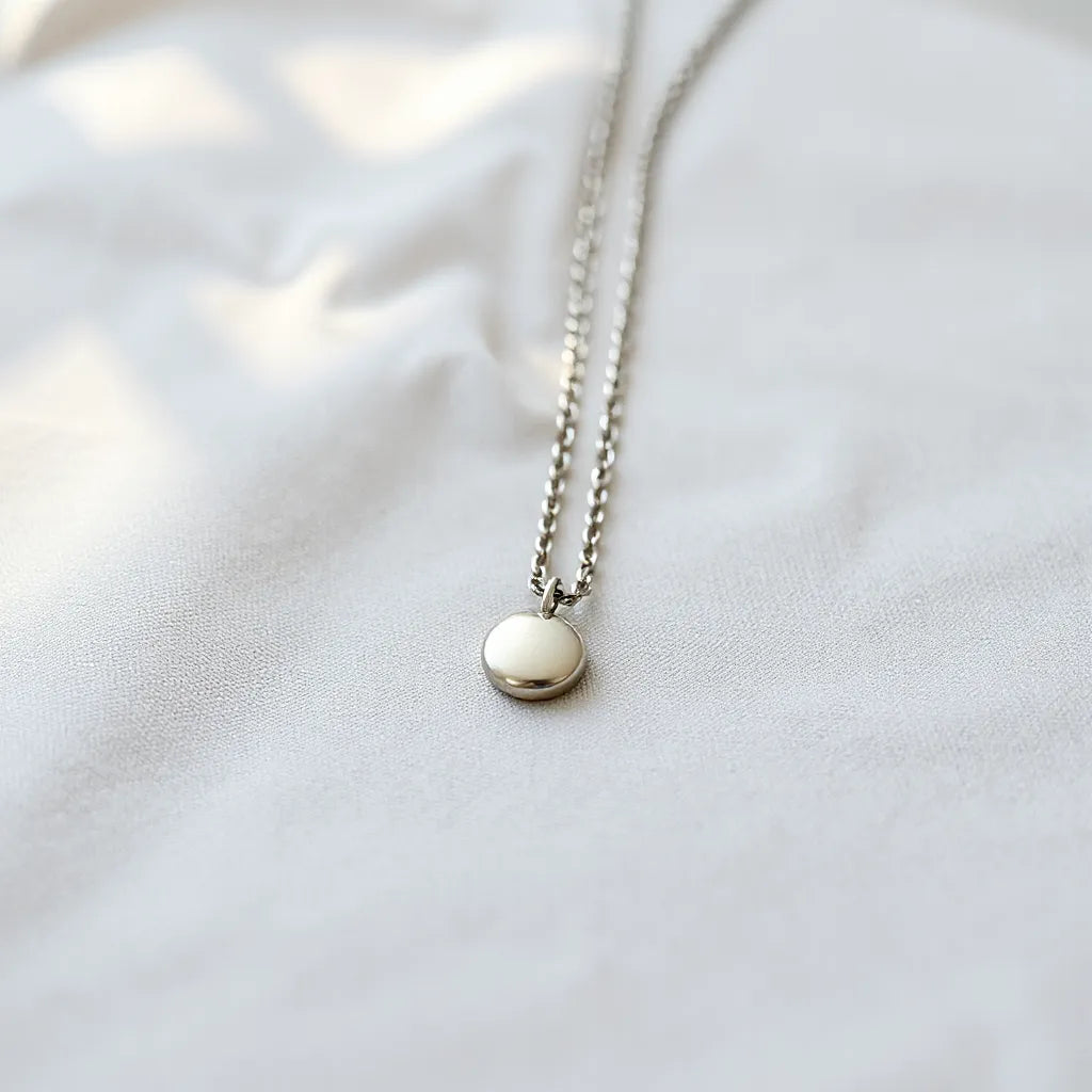 Polished silver necklace with a small pendant resting on light fabric in soft natural light