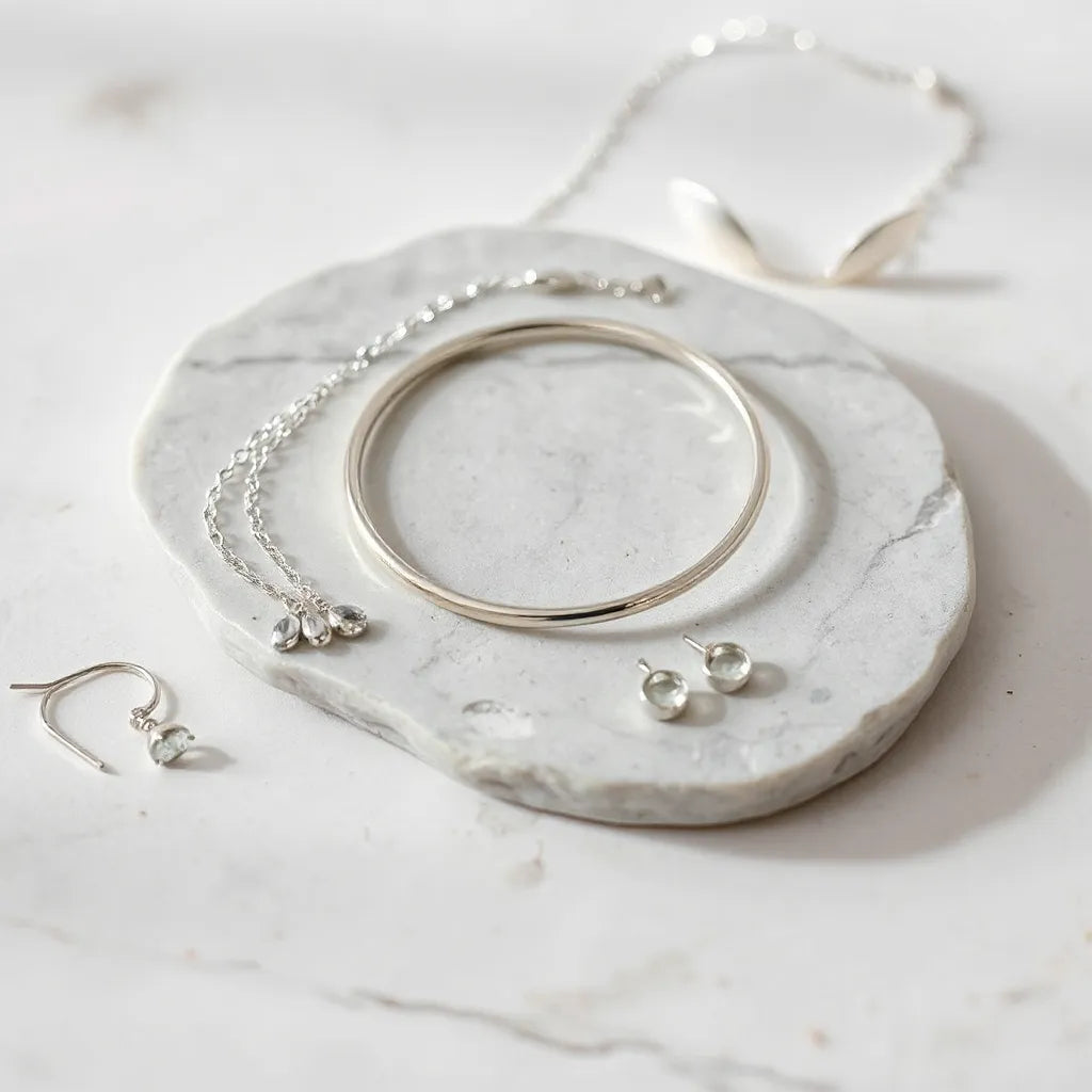 Polished silver necklace, bracelet, and earrings arranged on a light stone surface