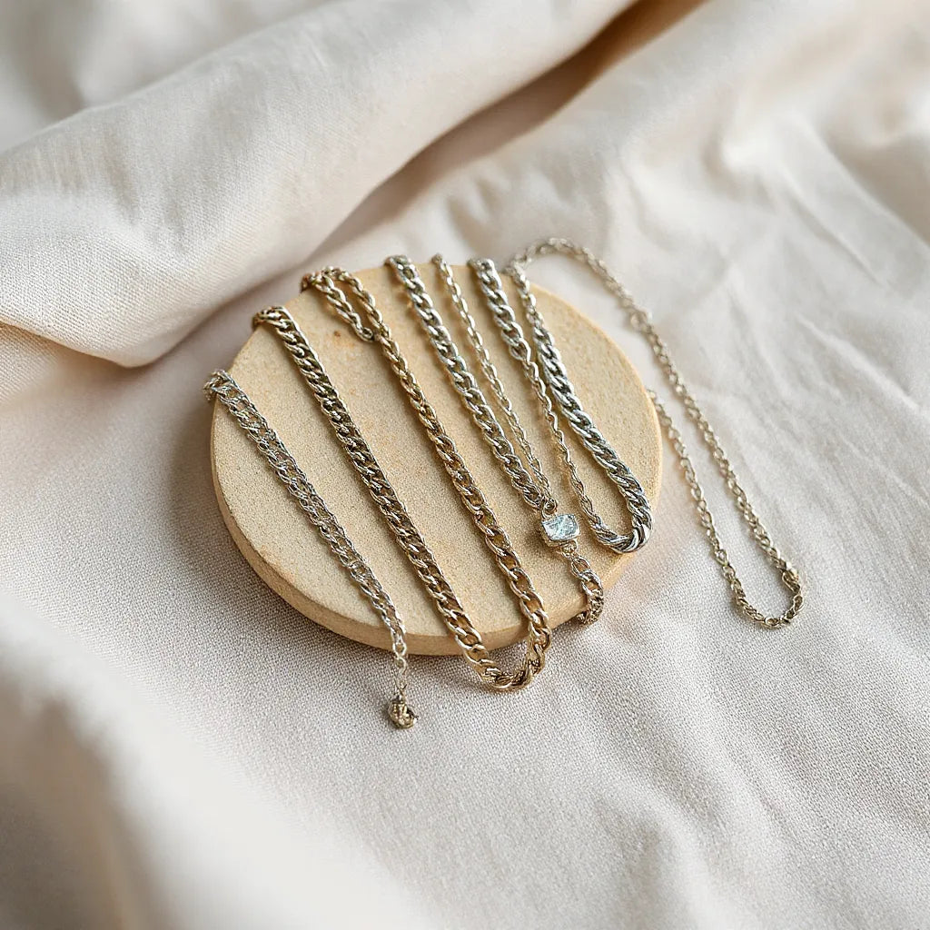 Assorted artisan silver chains with different links arranged on soft neutral fabric