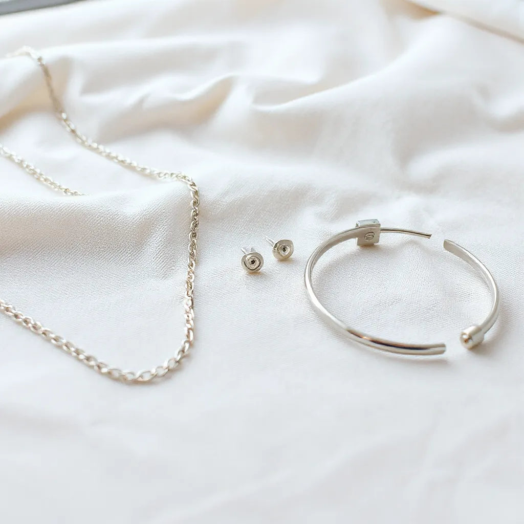 Polished classic silver necklace, stud earrings, and bracelet laid on neutral fabric