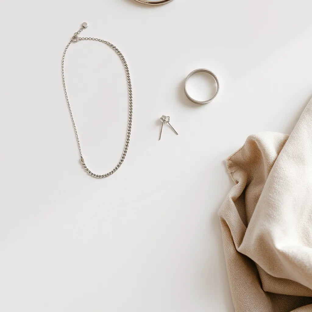 Silver necklace, bracelet, earrings, and ring arranged on a neutral background with soft scarf