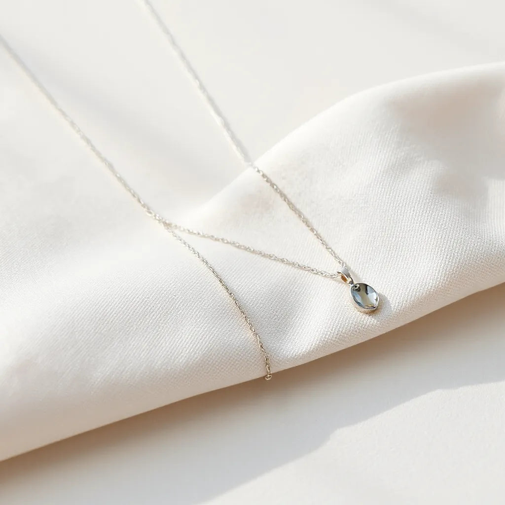 A delicate rhodium-finished necklace with a small pendant on neutral fabric under soft lighting