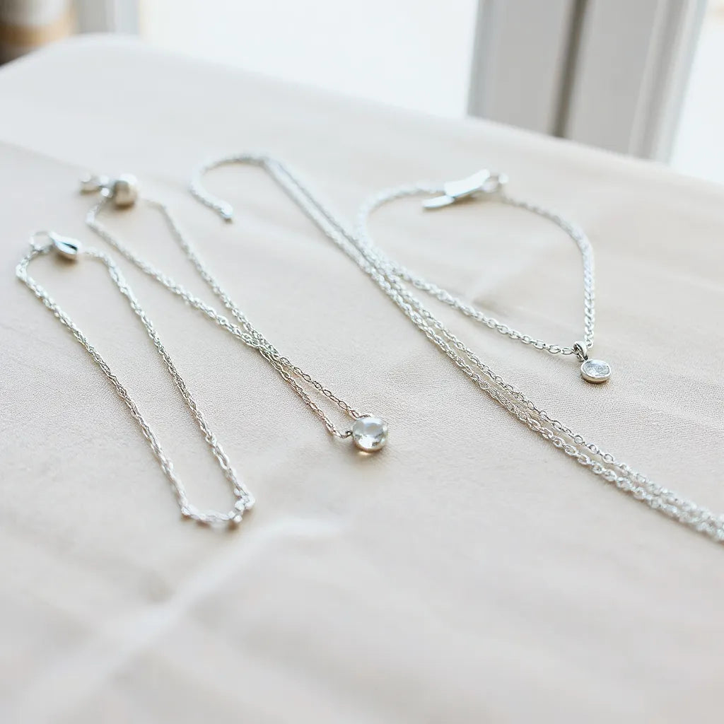 Layered designer silver necklaces arranged on neutral fabric with soft natural lighting