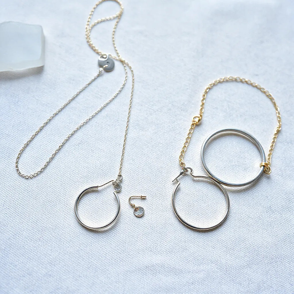 Sterling silver necklace, hoop earrings, and bracelet arranged on neutral fabric