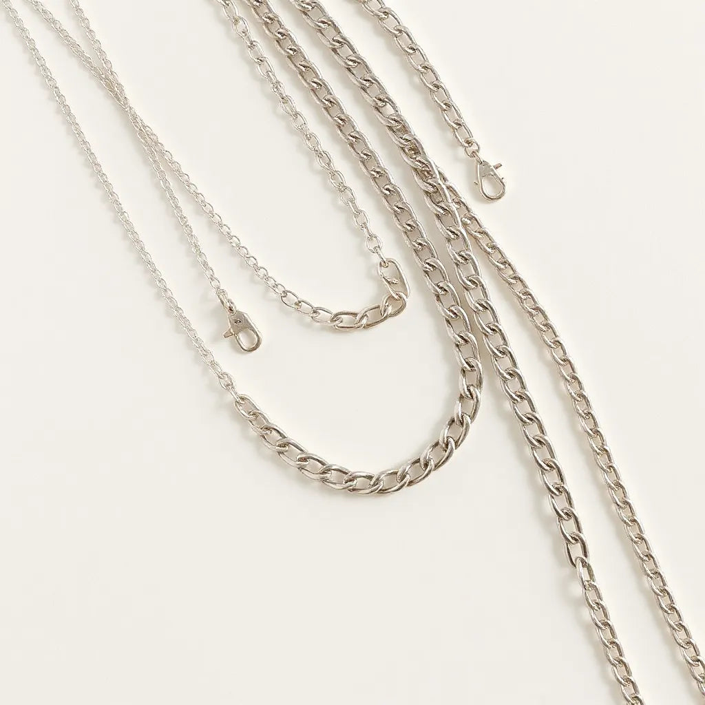Layered silver chains on a neutral background with soft light and visible metal shine.