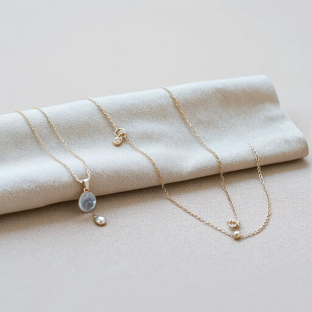 Multiple silver necklaces with delicate chains and small pendants arranged on soft neutral fabric