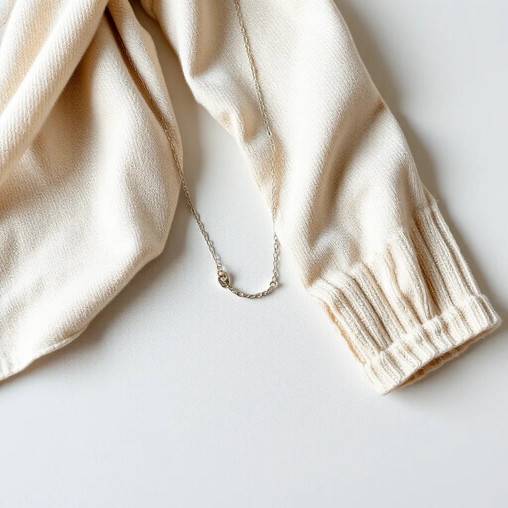 Lightweight silver necklace with a delicate chain resting on light fabric under soft natural light